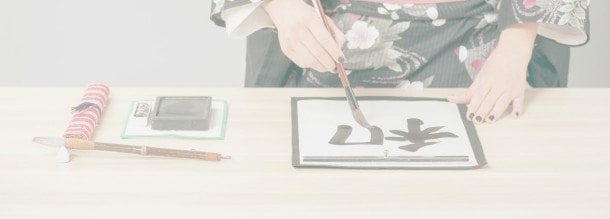 Woman in kimono writing. Closeup of a Japanese or Chinese woman writing hieroglyph in a traditional way with ink and brush while standing against table