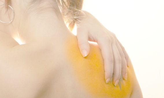 Photo showing the back of a woman with a sore shoulder. Her hand is on her shoulder.