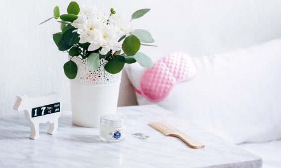 Bedside marble table with a white flower pot, a comb, two wedding rings and a clear cream jar.