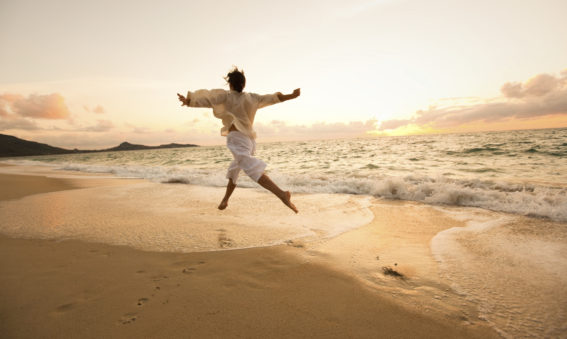 Woman embracing freedom, dancing along sandy beach with outstretched arms and waves at her feet