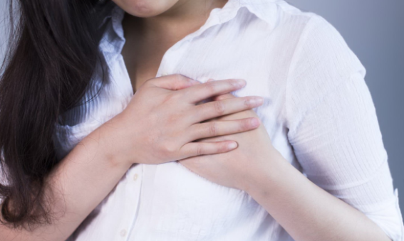 Woman in a white shirt holding both her hands close to her left breast