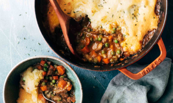 Shepherds pie consisting of mashed potato and a mixture of vegetables in a gravy underneath served in a casserole dish